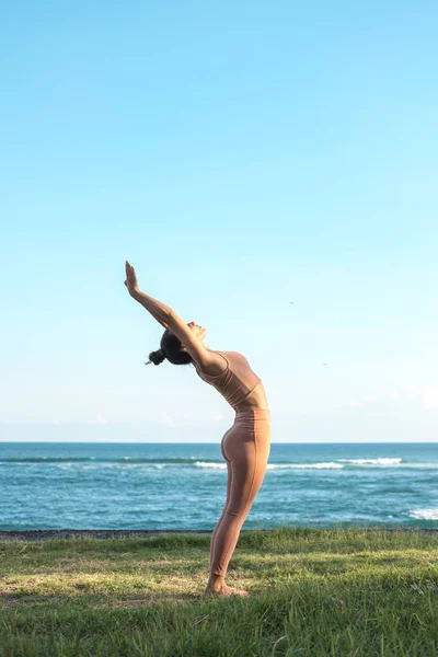 Eşofmanlı güzel genç bir kadın eğimlerini yaparken zarifçe eğiliyor. Kız okyanus kıyısındaki çimlere spor yapmaya gider. Tam boy dişi bir yogi yan yana durur..