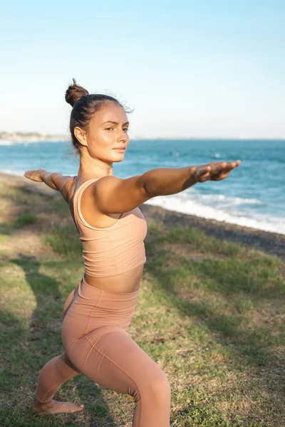 Savaşçı 2 egzersizinde duran barışçıl odaklı kız Virabhadrasana pozu, spor kıyafetleri giyiyor. Bali 'de bir kız okyanusta yoga yapıyor..