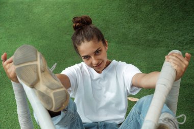 Atlıkarıncaya binen güzel bir genç kız. Mavi kotlu ve beyaz tişörtlü şık bir kız çimlerin üzerinde eğleniyor. Kadın şakacı görünüyor