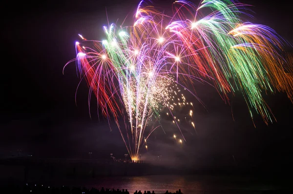 Colorful firework popping and lighting up the dark sky. Water reflection from coast.