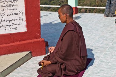 Kadın bir Budist rahibe Theravada yazısıyla taş bir levhanın önünde meditasyon yapıyor, Taung Kalat, Myanmar