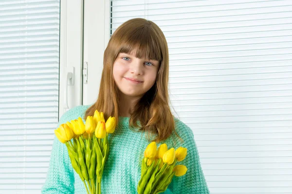 A little girl is sitting on the windowsill with a bouquet of tul — Stock Photo, Image