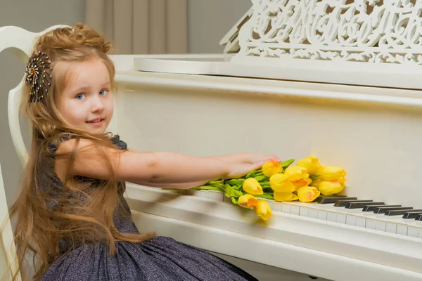 Flicka nära piano som ligger en bukett blommor. — Stockfoto