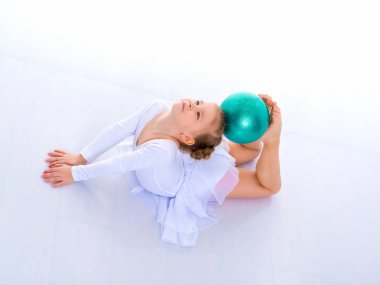 Küçük kız spor yapmak için büyük bir top üzerinde egzersiz yapıyor..