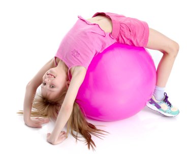 Küçük kız spor yapmak için büyük bir top üzerinde egzersiz yapıyor..