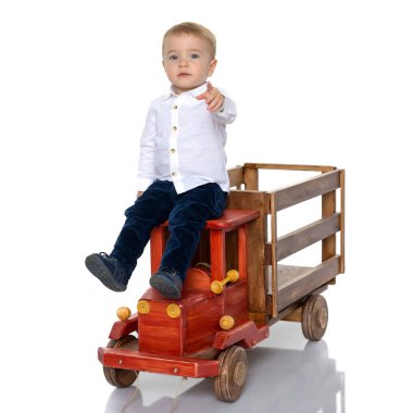 Şirin küçük çocuk, stüdyoda beyaz arka planda oyuncak ahşap bir arabayla oynuyor. Mutlu bir çocukluk, öğrenme ve eğitim kavramı. İzole edilmiş.