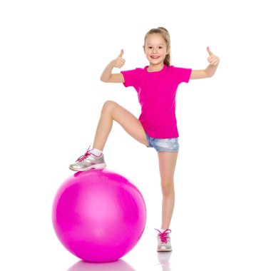 Küçük kız spor yapmak için büyük bir top üzerinde egzersiz yapıyor..