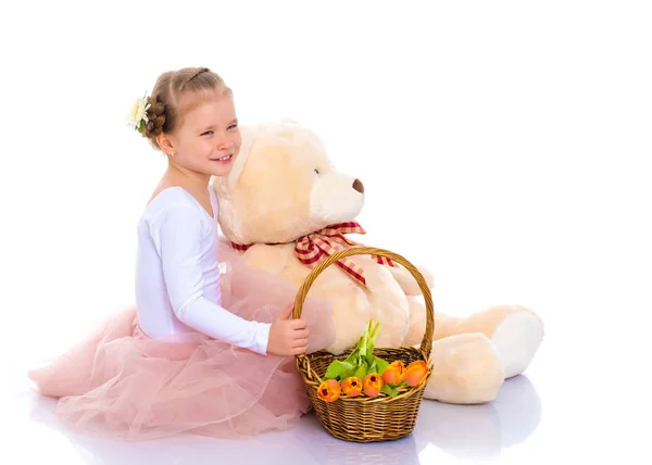 Een klein meisje met een mandje met bloemen en een teddybeer is sitti — Stockfoto