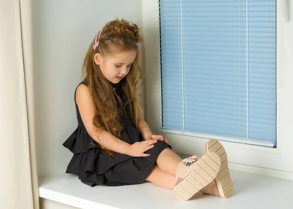 A little girl is sitting on the window on the background of the — Stock Photo, Image