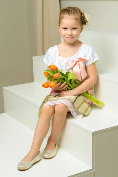 A little girl with a bouquet of tulips is sitting on the stairs. — Stock Photo, Image