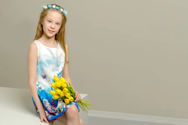 A little girl with a bouquet of tulips is sitting on the stairs. — Stock Photo, Image