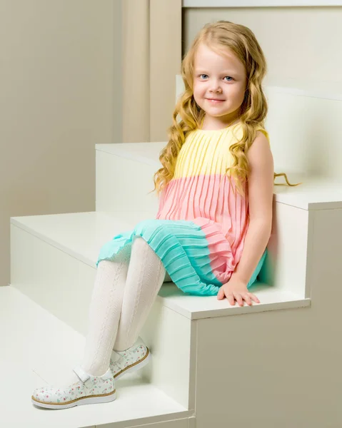Hermosa niña está sentada en la escalera blanca. — Foto de Stock