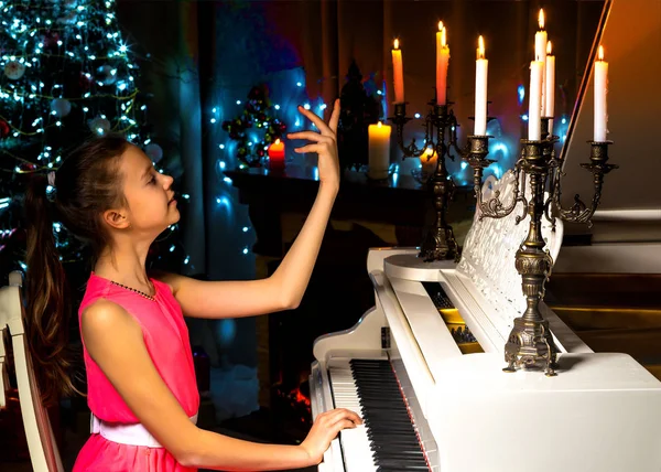 Девочка-подросток играет на пианино в рождественскую ночь при свечах — стоковое фото