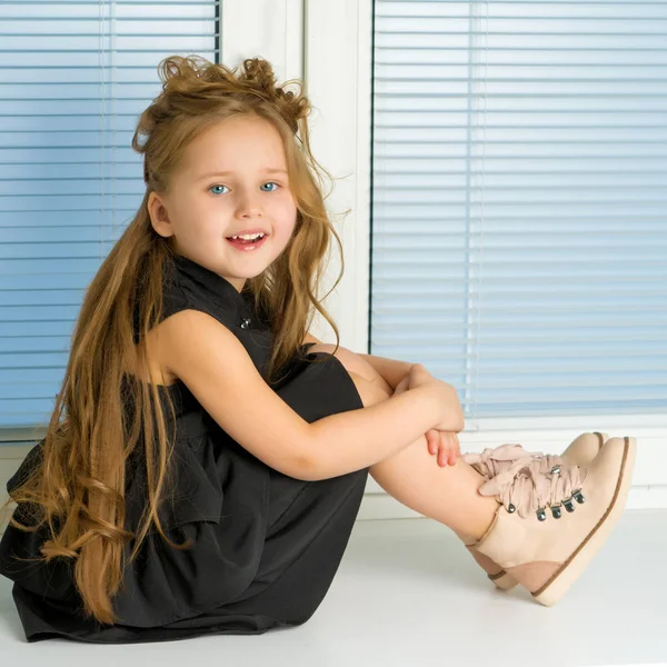 Malá holka sedí na okně na pozadí — Stock fotografie