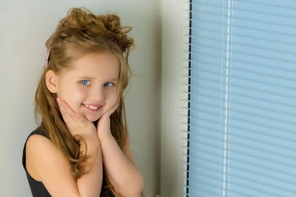 Una niña está sentada en la ventana en el fondo de la —  Fotos de Stock