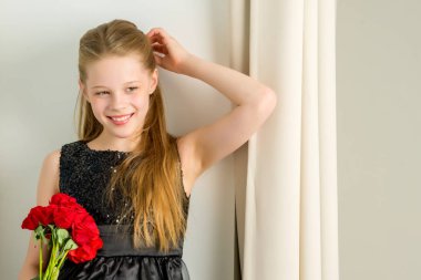 Küçük bir kız bir buket çiçek ile bir pencere pervazına oturur.