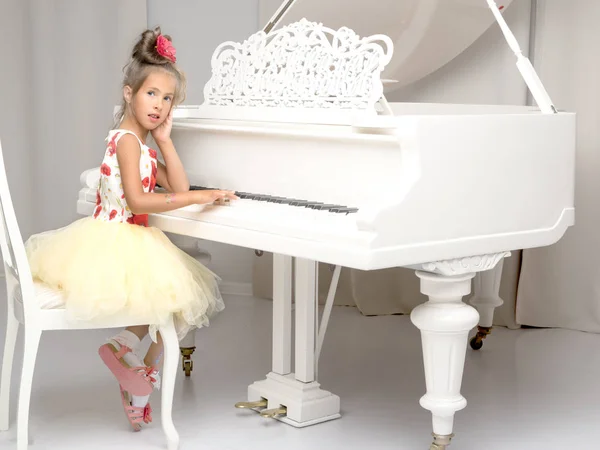 Beautiful little girl is playing on a white grand piano.