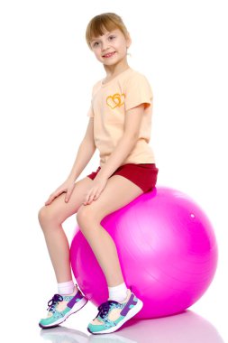 Küçük kız spor yapmak için büyük bir top üzerinde egzersiz yapıyor..