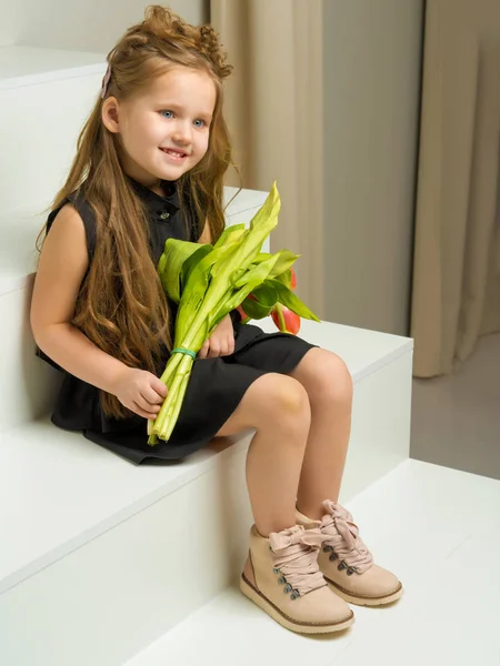 Een klein meisje met een boeket van tulpen zit op de trap. — Stockfoto
