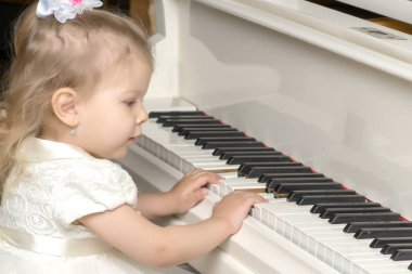 Güzel küçük kız beyaz bir piyanoda çalıyor..