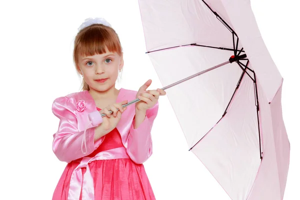 美しい少女は 短い前髪と頭に大きな白の弓です 赤いサテンのドレスとピンクのジャケット 女の子はピンクの傘を抱えてです — ストック写真