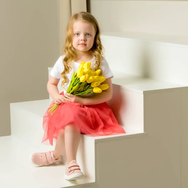 A little girl with a bouquet of tulips is sitting on the stairs. — Stock Photo, Image