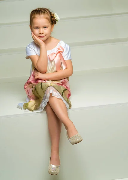 Schöne kleine Mädchen sitzt auf der weißen Treppe. — Stockfoto