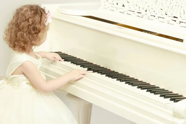 Beautiful little girl is playing on a white grand piano. — Stock Photo, Image