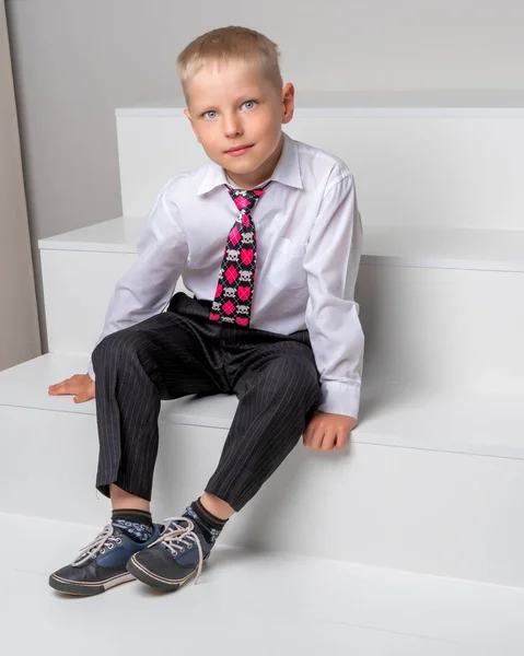 En liten pojke sitter på en vit trappa. — Stockfoto