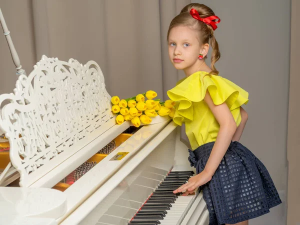 Girl schoolgirl near the piano on which lies a bouquet of flower — Stock Photo, Image