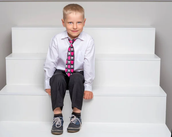 小さな男の子は白い階段に座っています。. — ストック写真