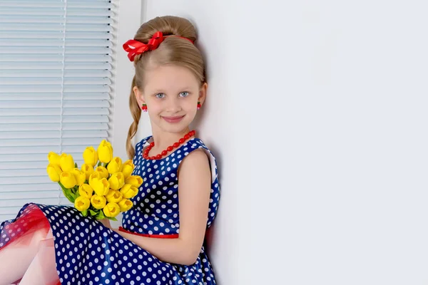 A little girl is sitting on the windowsill with a bouquet of tul — Stock Photo, Image