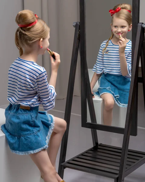 A little girl near the mirror paints lipstick lips — Stock Photo, Image