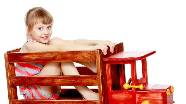 A menina está sentada em um grande carro de madeira de brinquedo . — Fotografia de Stock