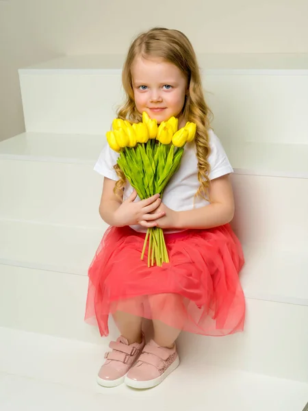 Een klein meisje met een boeket van tulpen zit op de trap. — Stockfoto