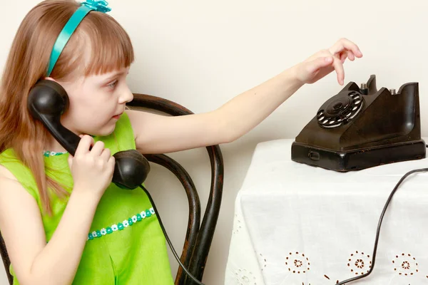 Pigen taler på en sort, gammel telefon med en roterende disk . - Stock-foto