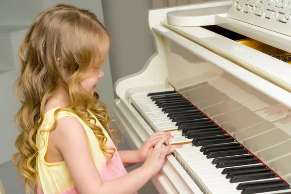 Güzel küçük kız beyaz bir piyanoda çalıyor..
