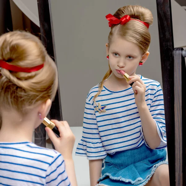 A little girl near the mirror paints lipstick lips — Stock Photo, Image