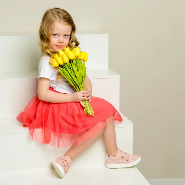 Lale bir buket ile küçük bir kız merdivende oturuyor. — Stok fotoğraf