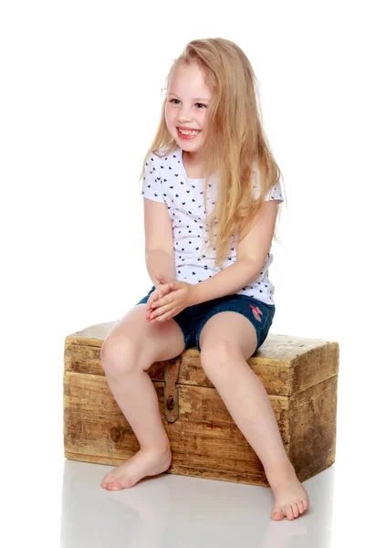 A little girl is sitting on a wooden box. — Stock Photo, Image