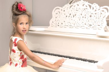 Güzel küçük kız beyaz bir piyanoda çalıyor..