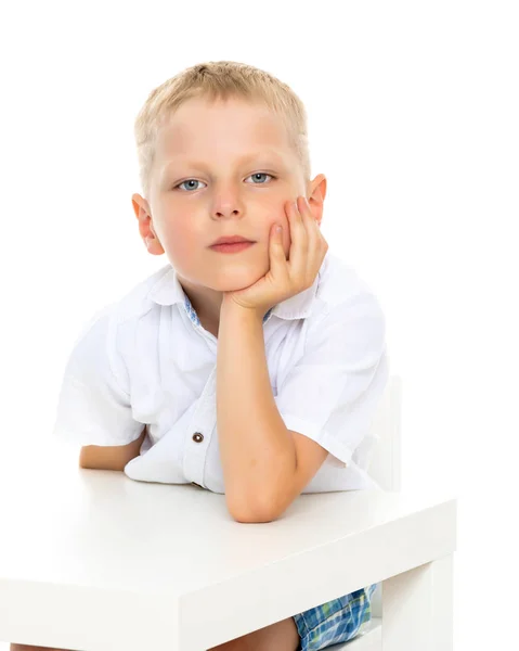 Um rapazinho está sentado à mesa . — Fotografia de Stock