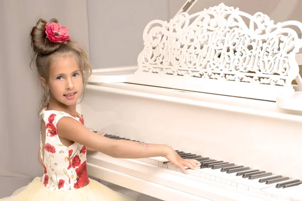 Güzel küçük kız beyaz bir piyanoda çalıyor..
