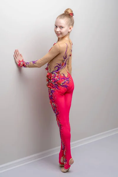 Little girl gymnast in a beautiful suit for competitions, posing in the studio near the wall. The concept of youth sports fashion, healthy lifestyle.
