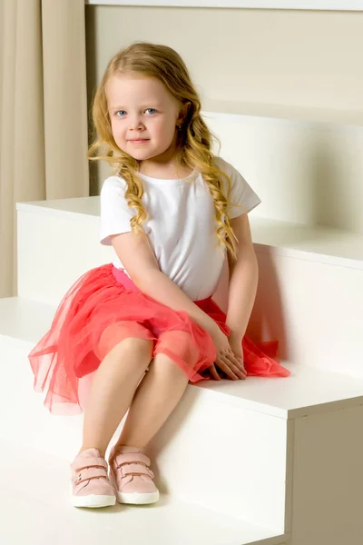 Krásná holčička sedí na bílém schodišti. — Stock fotografie