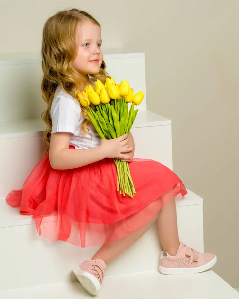 A little girl with a bouquet of tulips is sitting on the stairs. — Stock Photo, Image