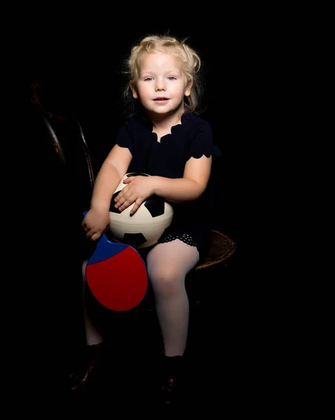 Menina com uma bola de futebol em um fundo preto . — Fotografia de Stock