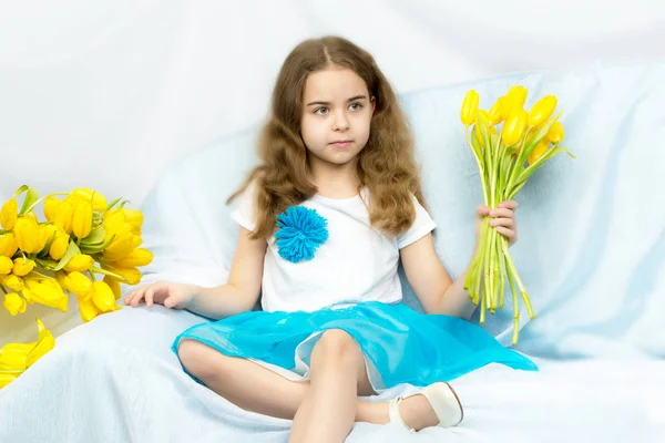 Mooie blonde schoolmeisje met gele tulpen zittend op de cou — Stockfoto