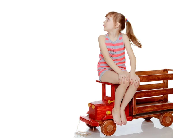 A menina está sentada em um grande carro de madeira de brinquedo . — Fotografia de Stock