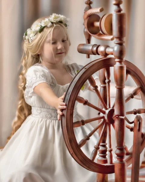 Uma menina bonito teceu uma lã com uma roda rotativa . — Fotografia de Stock